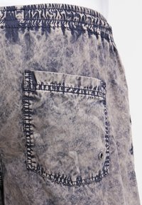 Shorts légers en tissu bleu-gris délavé. Dotés d'une taille élastique et d'une poche plaquée avec un bouton-pression en métal. Apparence texturée.