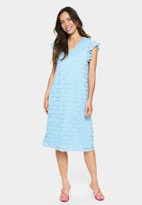 Rochie din dantelă de culoare bleu deschis, cu decolteu în V, mâneci scurte cu volane, tiv până la genunchi și model ondulat, asortată cu sandale roz.