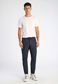 Marinefarbene Hose mit Kordelzugbund und schlanker Passform, kombiniert mit einem schlichten weißen T-Shirt mit Rundhalsausschnitt und weißen Sneakers mit farblichen Akzenten.