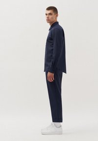 Camicia blu navy con bottoni, maniche lunghe e pantaloni dritti, abbinata a sneaker bianche. Tessuto dalla trama liscia, design minimalista.