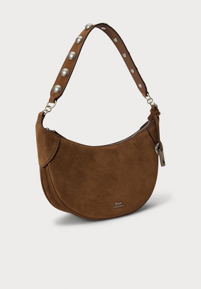 Brown suede shoulder bag with a curved shape, featuring a silver studded strap, zip closure, and logo detail on the front.