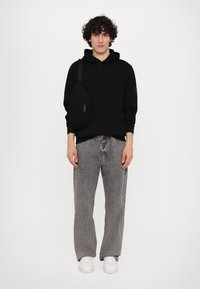 Felpa nera con cappuccio, jeans in denim grigi, sneakers bianche e una borsa a tracolla nera. Look casual; il tessuto sembra morbido e strutturato.