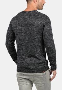 Grauer gestrickter Pullover mit strukturiertem Finish, rundem Ausschnitt und langen Ärmeln. Verfügt über ein kleines Logo-Tag am Saum. Getragen mit hellgrauen Hosen.