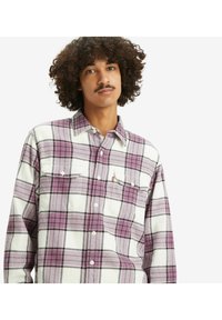 Koszula flanelowa w kratę w kolorze białym, purpurowym i czarnym. Długie rękawy, zapinana na guziki z dwoma kieszeniami na piersi. Miękka faktura i luźny krój.