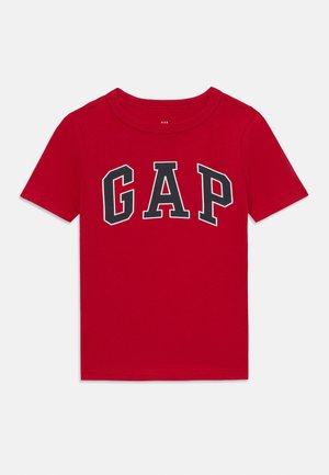 Camiseta de algodón roja con mangas cortas. Presenta un texto negro en negrita "GAP" en una fuente deportiva gruesa en el pecho. Diseño sencillo.
