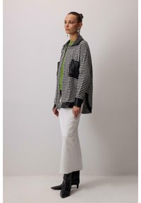Crna i bijela kaput u uzorku houndstooth, oversized kroja, s crnim kožnim detaljima, uparena s zelenom majicom i bijelim hlačama sa širokim nogavicama. Crne gležnjače.