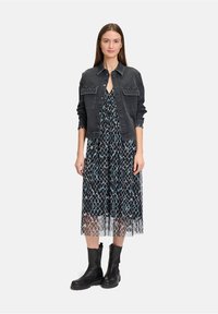 Czarna kurtka dżinsowa z akcentami w postaci ćwieków, nałożona na długą sukienkę w czarno-niebieski wzór. Modelka nosi czarne skórzane botki za kostkę.