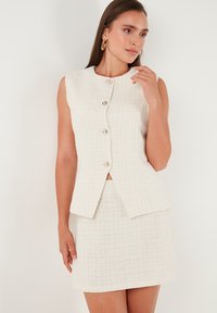 White textured two-piece outfit featuring a sleeveless top with button closure and a fitted mini skirt, both in a woven pattern.