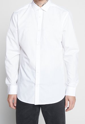 Biała koszula zapinana na guziki, wykonana z materiału mieszankowego, z klasycznym kołnierzykiem, długimi rękawami i zaokrąglonym dołem. Bez wzorów ani akcentów.