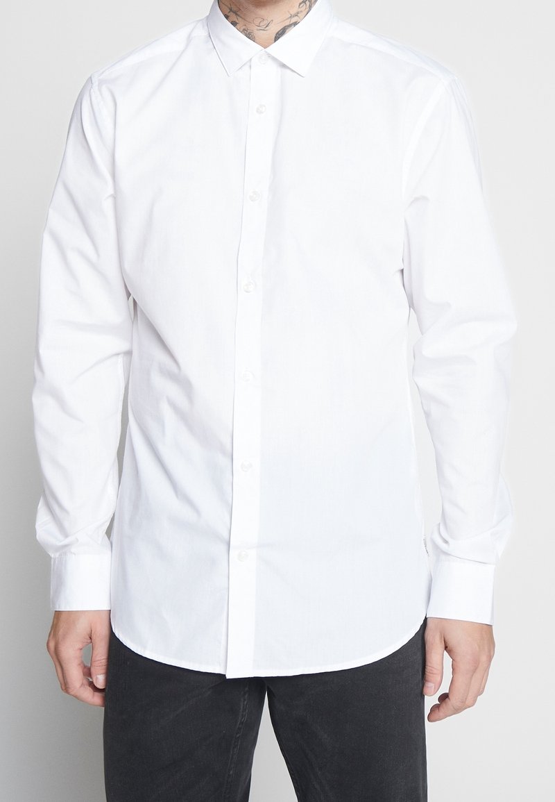 Camicia bianca con bottoni realizzata in tessuto misto cotone, con colletto classico, maniche lunghe e orlo curvo. Senza motivi né dettagli.