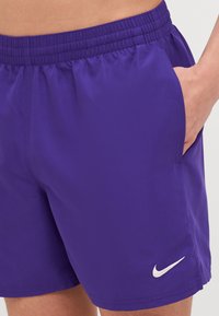Shorts de sport violets avec une taille élastique, dotés d'une poche latérale et d'un logo Nike blanc au bas. Texture de tissu lisse.