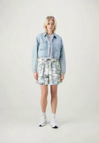 Light blue denim cropped jacket over a white shirt, paired with a floral-patterned elastic waist skirt and white sneakers.