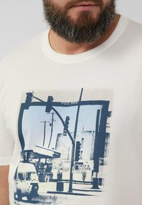 Cream-colored t-shirt featuring a graphic print of a street scene with traffic lights and a vintage vehicle in blue tones.