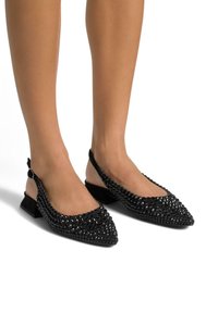 Des chaussures à talon ouvert noires avec des pointes pointues, présentant une surface texturée de clous noirs et un petit talon carré pour le soutien.