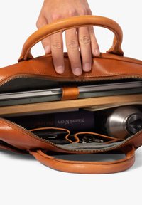 Brown leather bag with two handles, showcasing an open top revealing a laptop, books, a water bottle, and various other items inside.
