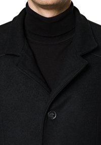 Czarny wełniany płaszcz z wyciętym kołnierzem, z jednobutonowym zapięciem i czarnym, prążkowanym golfem pod spodem. Gładka faktura i dopasowany krój.