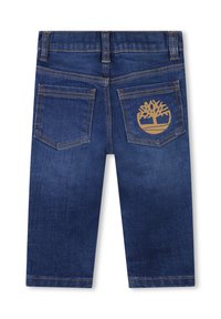 Jeans para niños pequeños de color azul oscuro con dos bolsillos traseros, uno de los cuales cuenta con un logo de árbol marrón y costuras naranjas a lo largo de las costuras y bolsillos.