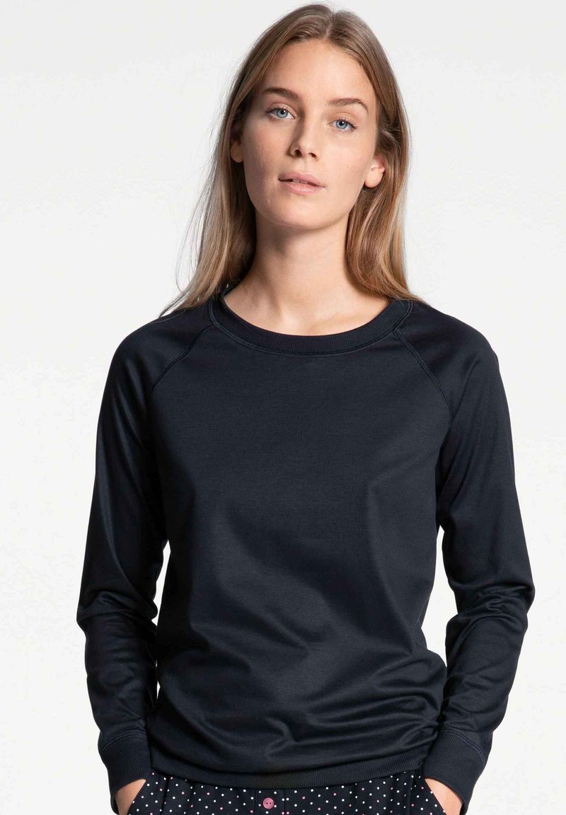 Black long-sleeve sweatshirt with a round neckline and ribbed cuffs. Smooth texture and fitted design, paired with patterned bottoms.