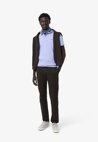 Paita polo vaaleansinisena kauluksella, yhdistettynä tummaan neuleeseen, joka on heitetty hartioille ja mustiin housuihin. Asusteina on sininen kuviollinen huivi.