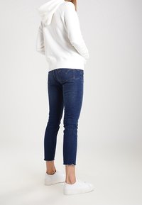 Felpa bianca con cappuccio, jeans in denim blu con orli sfrangiati e sneakers bianche, viste da dietro.