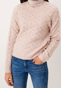 Pull tricoté rose clair avec motif en losanges, poignets et ourlet côtelés, associé à un jean en denim bleu. La texture semble douce et confortable.