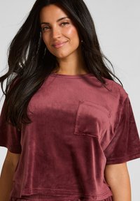 Korte mouwen, bordeaux top in een zachte, fluwelen stof met een borstzak en ronde halslijn. Ontworpen voor een casual pasvorm.