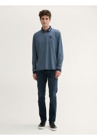 Granatowa polo z długim rękawem i prążkowanym kołnierzykiem, w połączeniu z ciemnoniebieskimi dżinsami i czarnymi sneakersami, z małym logo na piersi.