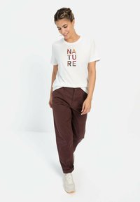 Hvid kortærmet skjorte med "NATURE" trykt i flerfarvede bogstaver, parret med mørk burgunder bukser og lyse sneakers. Casual pasform.