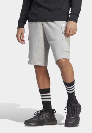Szare szorty z mieszanki bawełny z bocznymi kieszeniami, w połączeniu z czarnymi butami sportowymi i czarnymi skarpetkami z trzema białymi paskami.