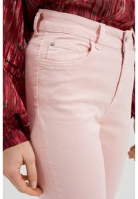 Vaaleanpunaiset farkut, joissa on istuva malli, etutasku ja ommeltu yksityiskohtia. Kangas on pehmeä rakenne ja hienovarainen kiilto.