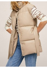 Beige puffer vest with a high collar, front pocket, and side zipper, featuring horizontal quilted sections and a smooth, shiny texture.