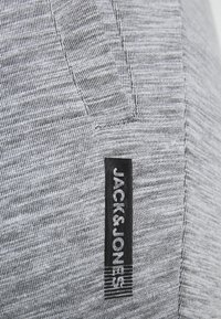Grå struktureret stof med fine striber, udstyret med et sort mærke med teksten "JACK & JONES" og vandrette accenter nederst.