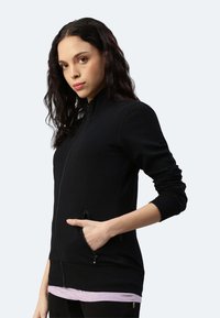 Giacca nera con zip e colletto alto, realizzata in un tessuto liscio, dotata di tasche laterali e polsini a coste per un look aderente.