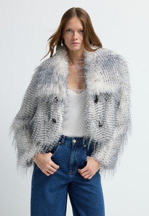 Faux fur jacket with a gray and white pattern, featuring a shaggy texture, double-breasted design, and two black buttons. Paired with blue jeans.