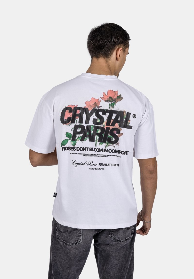 Bílý tričko s multikolorovým květinovým designem na zadní straně a černým textem. Krátké rukávy, kulatý výstřih a volný střih.