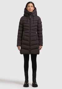 Padded dark brown coat with a high collar, front zipper, drawstrings, and side pockets; fitted with long sleeves and a knee-length design.