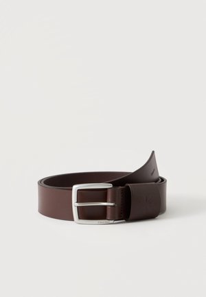 Ceinture en cuir marron foncé roulée avec boucle rectangulaire argentée et logo discret Calvin Klein sur la boucle en cuir, présentée sur fond blanc.