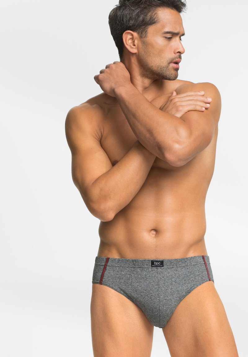 Slip grigi in cotone con design aderente, caratterizzati da dettagli laterali rossi e una fascia nera con logo. Texture liscia, stile minimalista.