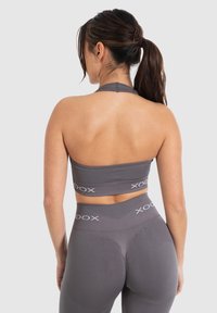 Conjunto de ropa deportiva gris que incluye un top deportivo con cuello halter y leggings de cintura alta, ambos confeccionados con una tela suave y elástica y acentos de logo.