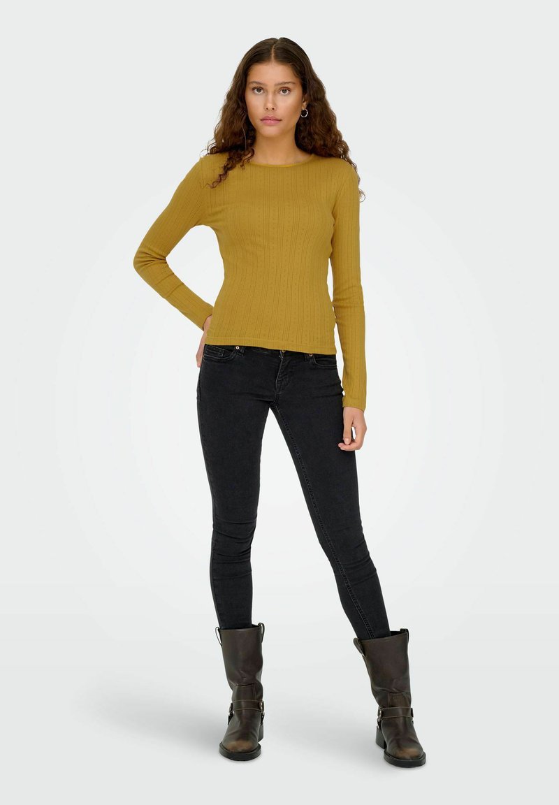 Sennepsfarvet ribbet langærmet top, tætsiddende design, parret med sorte skinny jeans og brune ankelstøvler med spænde detaljer.