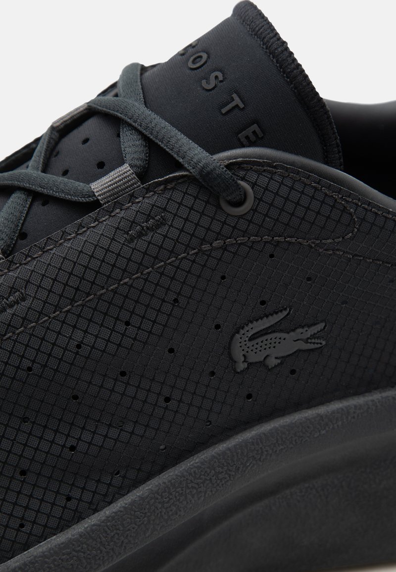 Sneaker nero Lacoste con motivo testurizzato, perforazioni, lacci neri, logo coccodrillo in rilievo e marchio "LACOSTE" sulla linguetta.