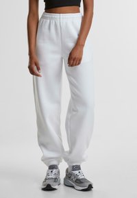 Witte joggerpants van zachte stof, met een elastische tailleband en boorden, in een relaxte pasvorm en minimale textuurdetails.