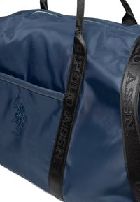 Navy blue duffel bag made of glossy nylon, featuring a front pocket, textured black straps with "USPA" branding, and a raised logo detail.