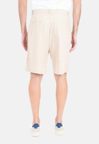 Shorts in cotone beige con vita elastica, dotati di due tasche posteriori e una lunghezza fino al ginocchio. Indossati con sneakers bianche e blu.