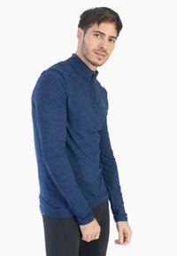 Maglietta a maniche lunghe blu navy con colletto alto e design con zip a quarto, realizzata in tessuto testurizzato e traspirante. Presenta maniche aderenti.