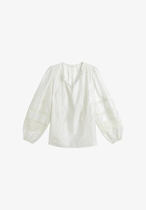 Blouse blanche à manches longues avec inserts en dentelle sur les manches, encolure à cordon de serrage et manches amples et bouffantes se terminant par des poignets élastiques.