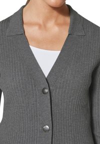 Grijze geribbelde cardigan met een V-hals, voorzien van een set van drie donkere knopen aan de voorkant. Gemaakt van zachte, gestructureerde stof.