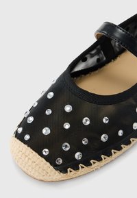 Chaussure espadrille noire à tige en maille, ornée de strass transparents, avec une semelle en jute tissée. Comprend une bride noire assortie.