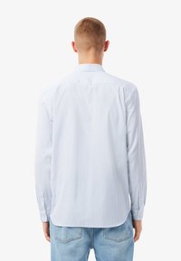 Camisa de manga larga a rayas azul claro con dobladillo curvado, puños abotonados y cuello clásico; confeccionada en una tela suave y ligera.