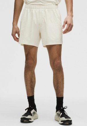 Kremfarvede bomuldsshorts med elastisk talje, der har en afslappet pasform og en glat, let tekstur. Bruges sammen med sorte sneakers.